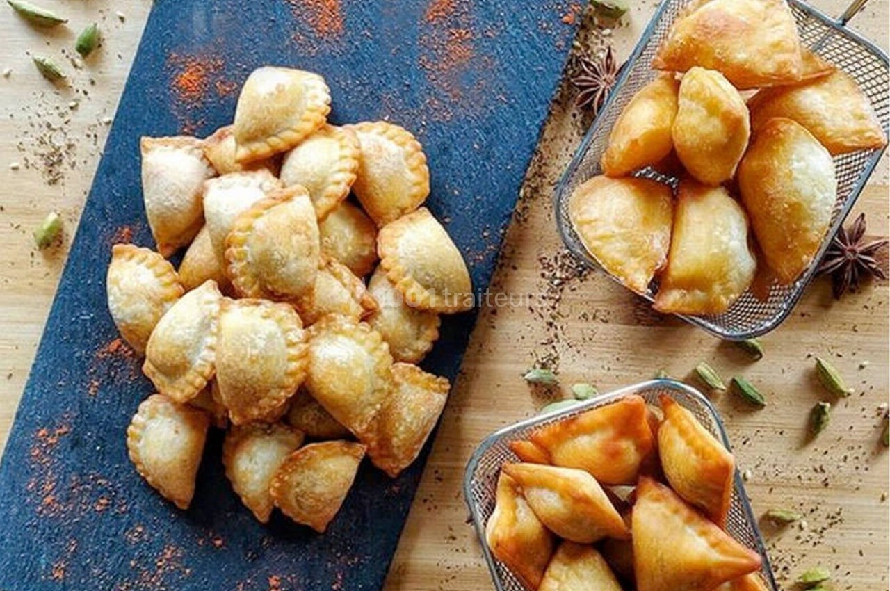 Assortiment de beignets dorés disposés sur une ardoise et dans des paniers métalliques, entourés d'épices.