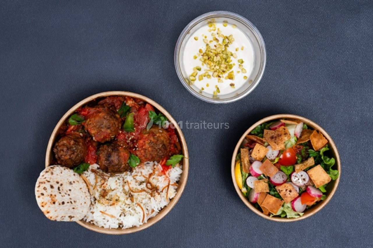Assiette avec boulettes, riz, pain plat, salade colorée et bol de yaourt garni de pistaches, sur fond sombre.