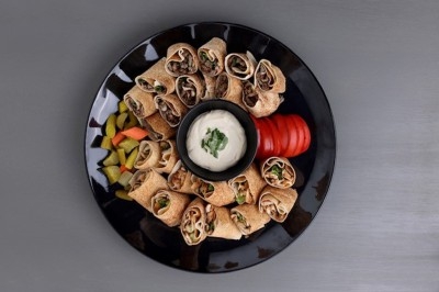 Miniature Traiteur Saint-Denis (Seine-Saint-Denis) - Leon Catering Libanais  #23 Assiette de wraps garnis autour d'un bol de sauce blanche, accompagnée de légumes marinés et de tranches de tomate.