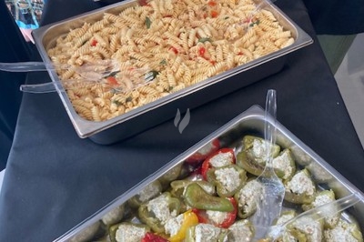 Assiette noire contenant des wraps garnis, accompagnée de légumes, de tranches de tomate et d'une sauce blanche au centre.