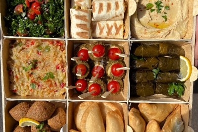 Assiette noire contenant des wraps garnis, accompagnée de légumes, de tranches de tomate et d'une sauce blanche au centre.