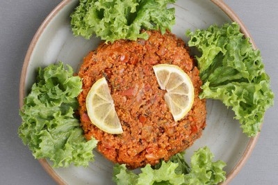 Assiette noire contenant des wraps garnis, accompagnée de légumes, de tranches de tomate et d'une sauce blanche au centre.