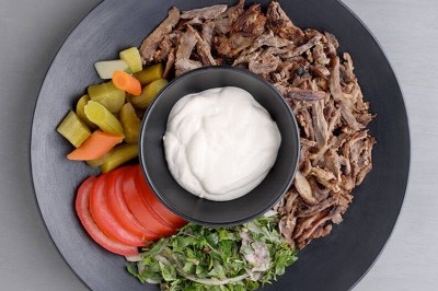 Assiette noire contenant des wraps garnis, accompagnée de légumes, de tranches de tomate et d'une sauce blanche au centre.