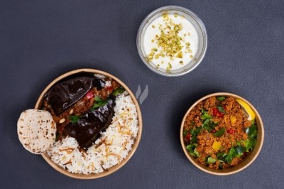 Assiette noire contenant des wraps garnis, accompagnée de légumes, de tranches de tomate et d'une sauce blanche au centre.