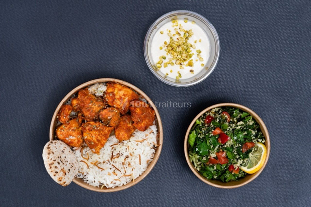 Plat composé de poulet épicé, riz, pain plat, salade taboulé et sauce blanche garnie de pistaches.