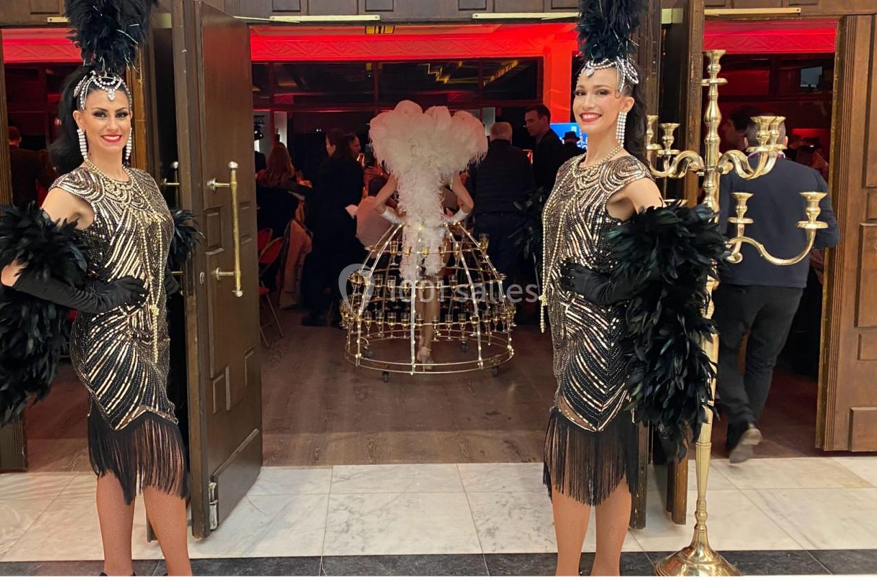 Deux danseuses en tenue à plumes et perles accueillent les invités dans un lieu éclairé de lumières rouges.