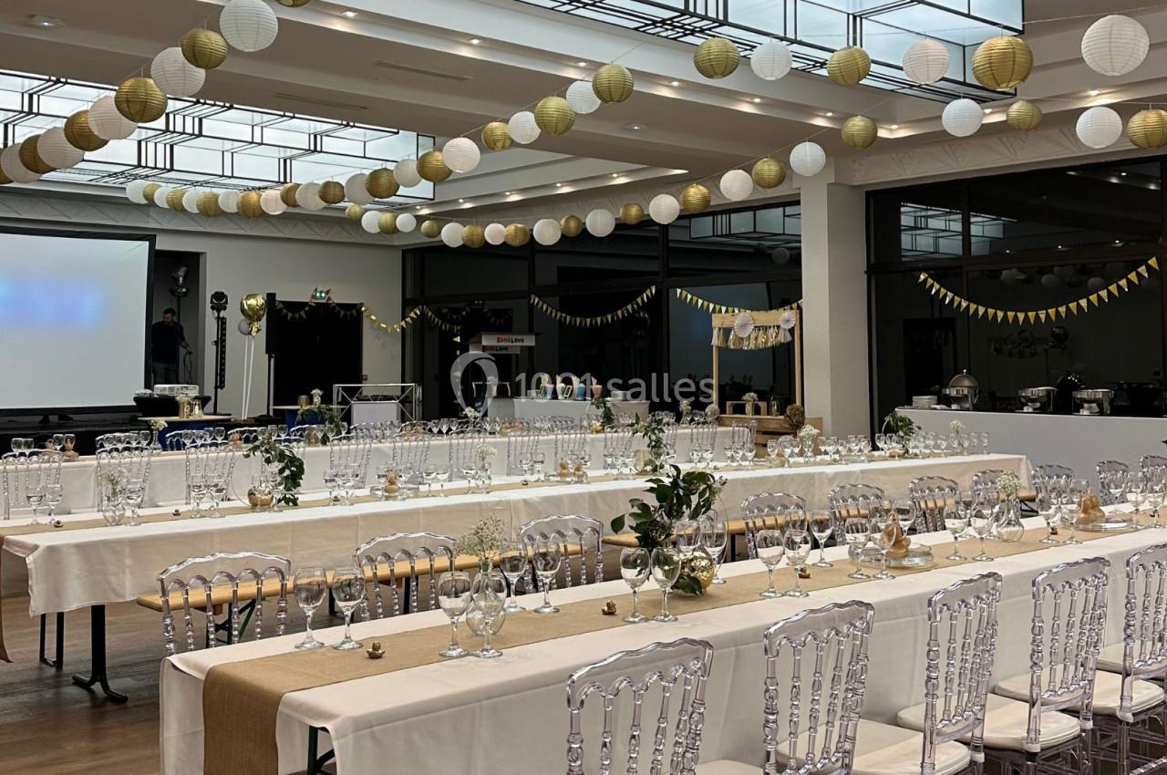 Salle de réception décorée avec des guirlandes et des tables dressées pour un événement festif.