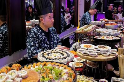 Entrée d'un bâtiment blanc entouré d'arbres, avec des portes vitrées illuminées par une lumière intérieure.