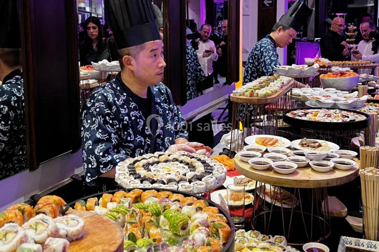Un chef prépare et présente un buffet varié de sushis et plats japonais dans un cadre élégant.