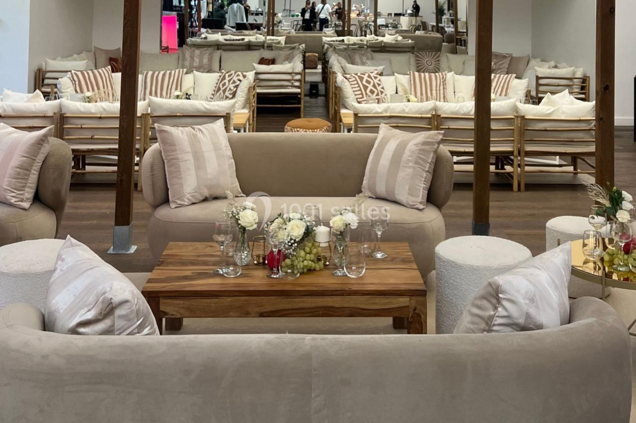 Salon élégant avec canapés beiges, table basse en bois décorée de fleurs et verres, dans un espace lumineux et moderne.
