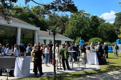 Entrée d'un bâtiment blanc entouré d'arbres, avec des portes vitrées illuminées par une lumière intérieure.