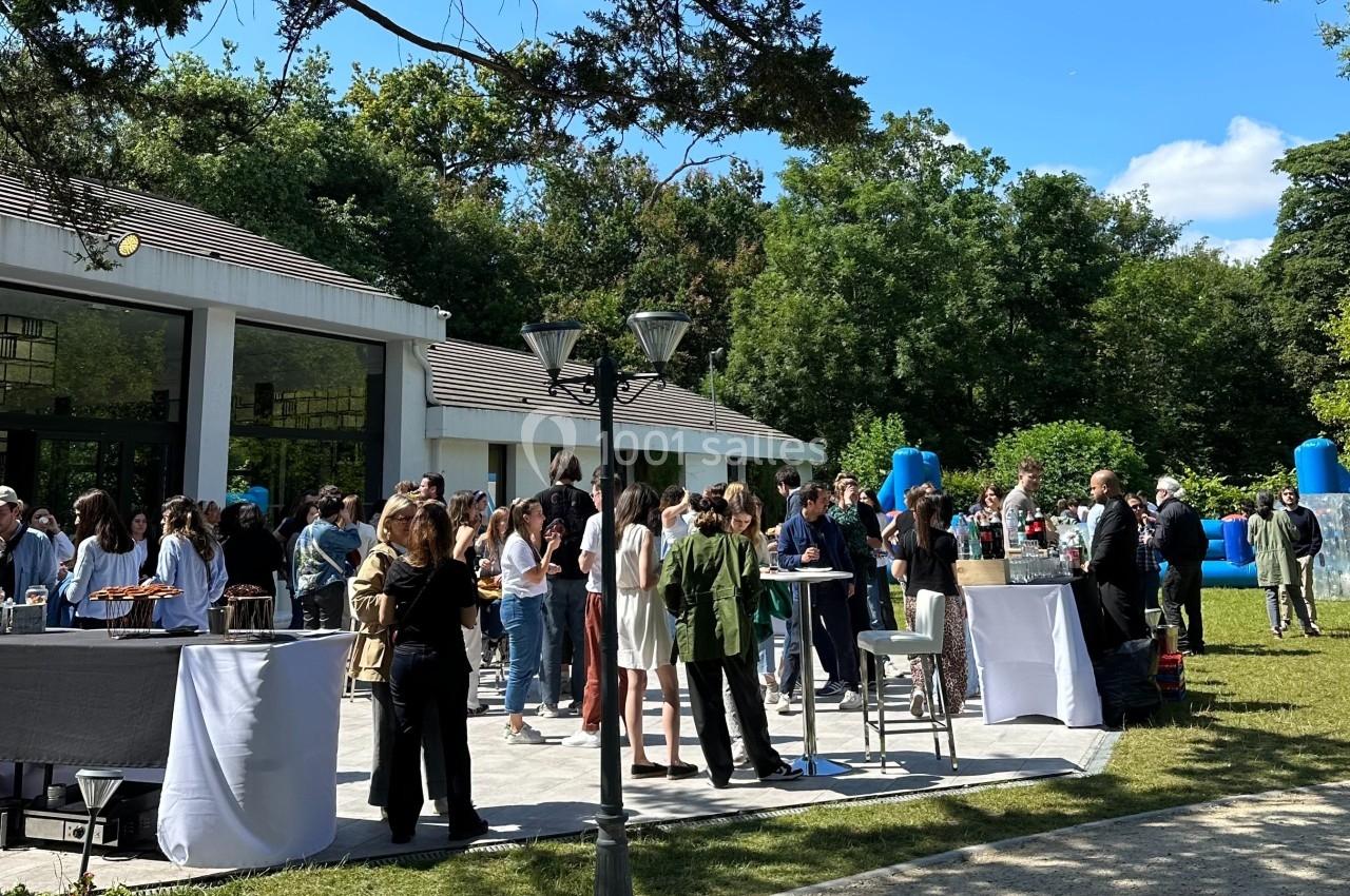 Groupe de personnes rassemblées en extérieur près d'un bâtiment, discutant autour de tables lors d'un événement.