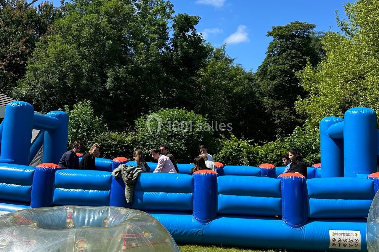 Des personnes interagissent sur une structure gonflable bleue en plein air, entourée de végétation.