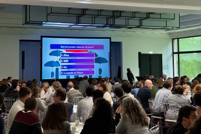 Entrée d'un bâtiment blanc entouré d'arbres, avec des portes vitrées illuminées par une lumière intérieure.