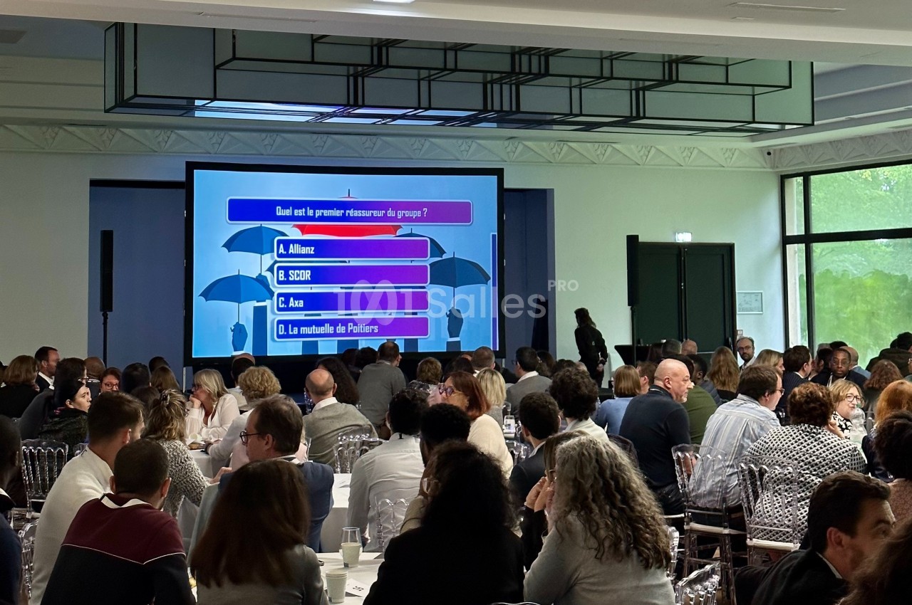 Des personnes assistent à un quiz interactif projeté sur un écran dans une salle de conférence lumineuse.