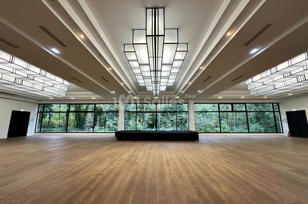 Salle spacieuse avec parquet en bois, grandes baies vitrées donnant sur un espace vert et plafonniers géométriques.