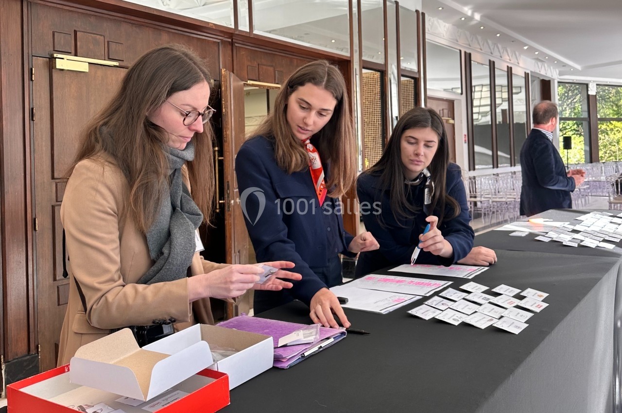 Trois femmes organisent des badges sur une table lors d'un événement dans un espace intérieur lumineux.