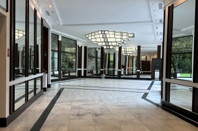 Entrée d'un bâtiment blanc entouré d'arbres, avec des portes vitrées illuminées par une lumière intérieure.