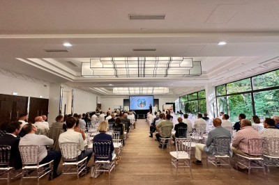 Entrée d'un bâtiment blanc entouré d'arbres, avec des portes vitrées illuminées par une lumière intérieure.