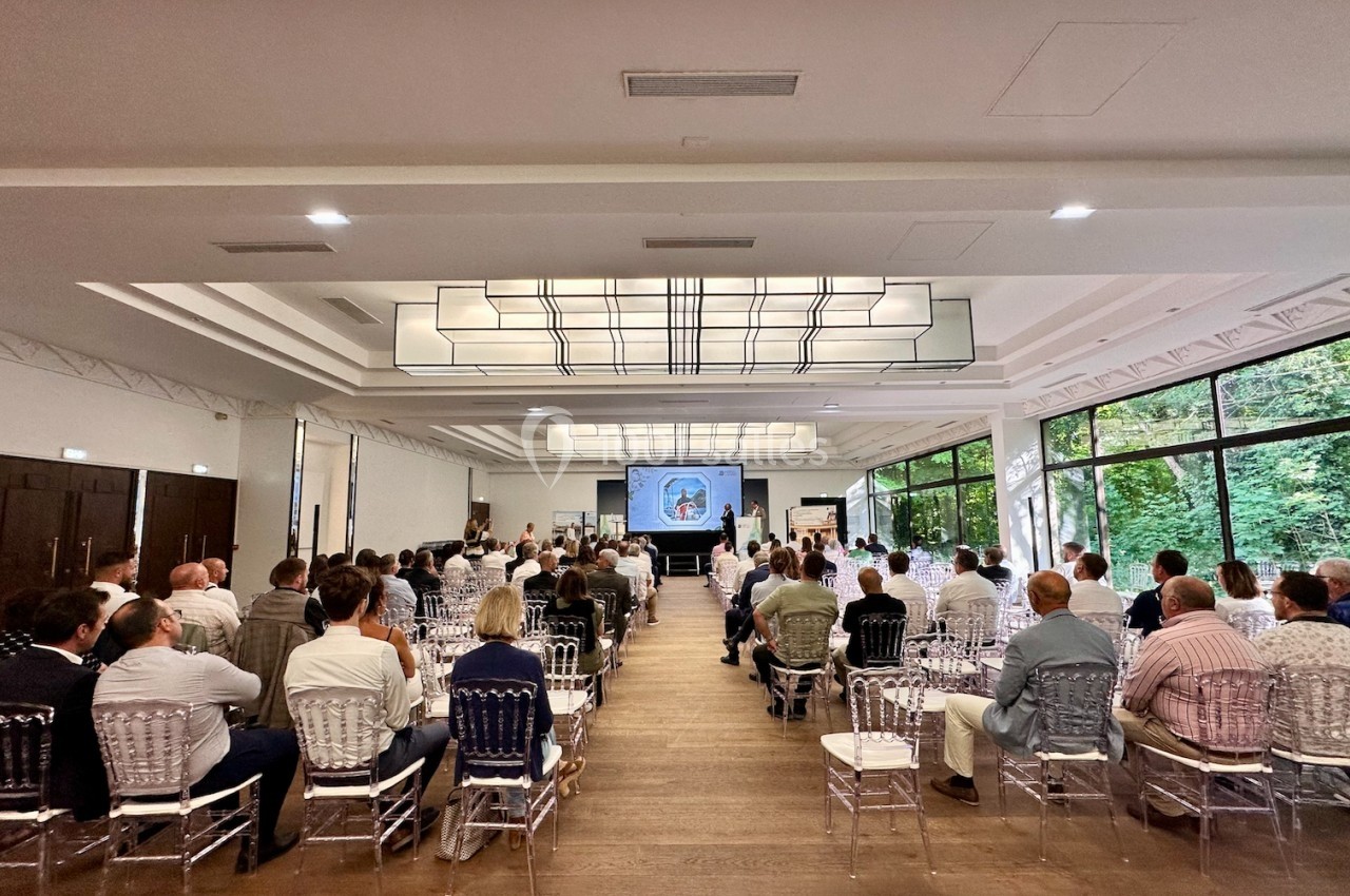 Salle de conférence lumineuse avec des participants assis, regardant une présentation projetée sur un écran.