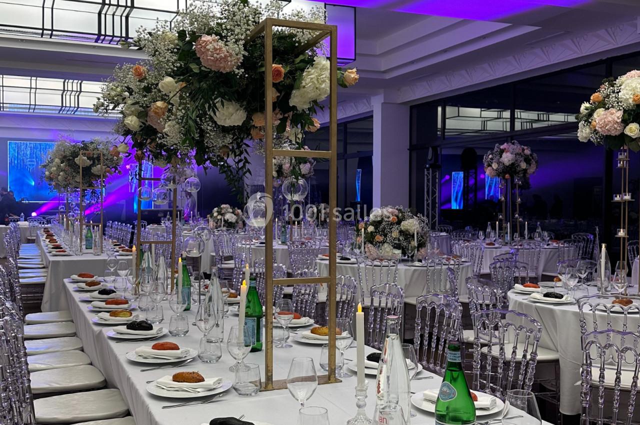 Salle de réception décorée avec des tables dressées, des chandeliers fleuris et un éclairage violet en arrière-plan.