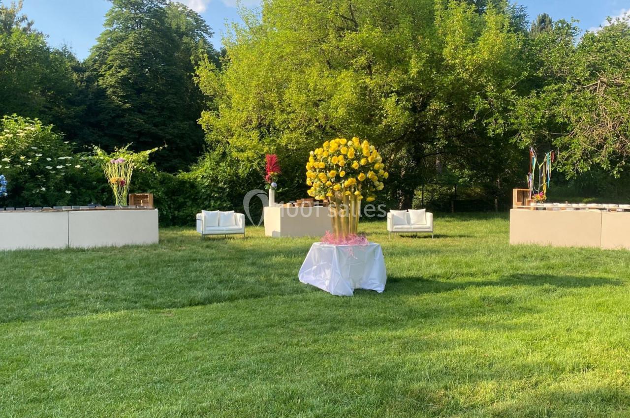 Arrangement floral coloré sur une pelouse verdoyante, entouré de buissons et d'arbres sous un ciel clair.