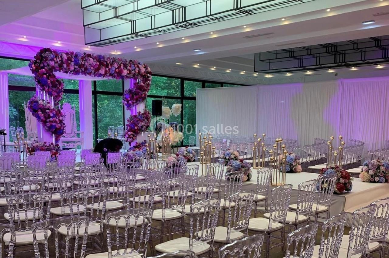 Salle de réception décorée pour un mariage avec des chaises transparentes, des fleurs et des bougies.