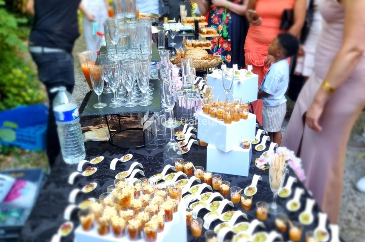 Buffet en extérieur avec verrines, amuse-bouches et verres disposés sur une table noire, entourée de convives.