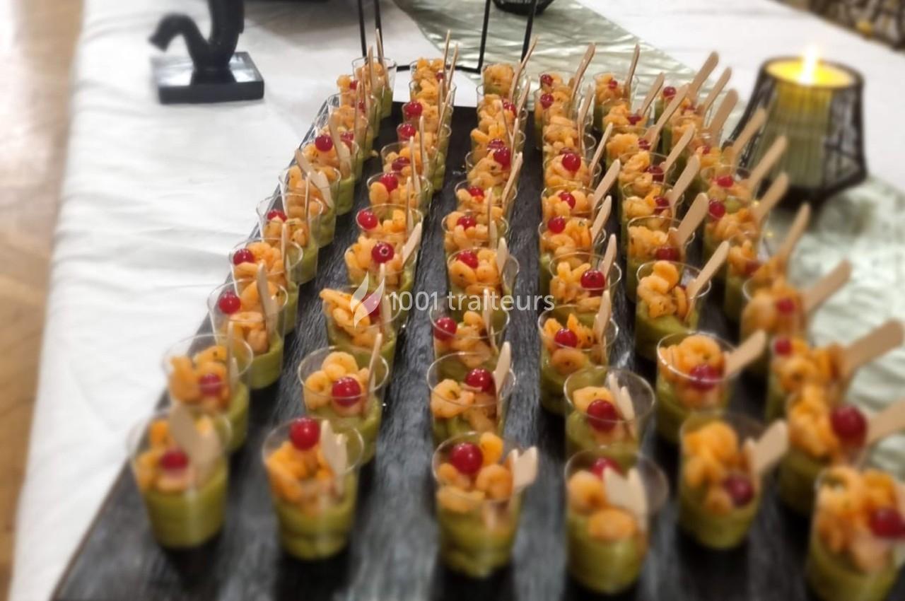 Verrines alignées sur un plateau, contenant des crevettes, de l'avocat et des tomates cerises, avec des cuillères en bois.