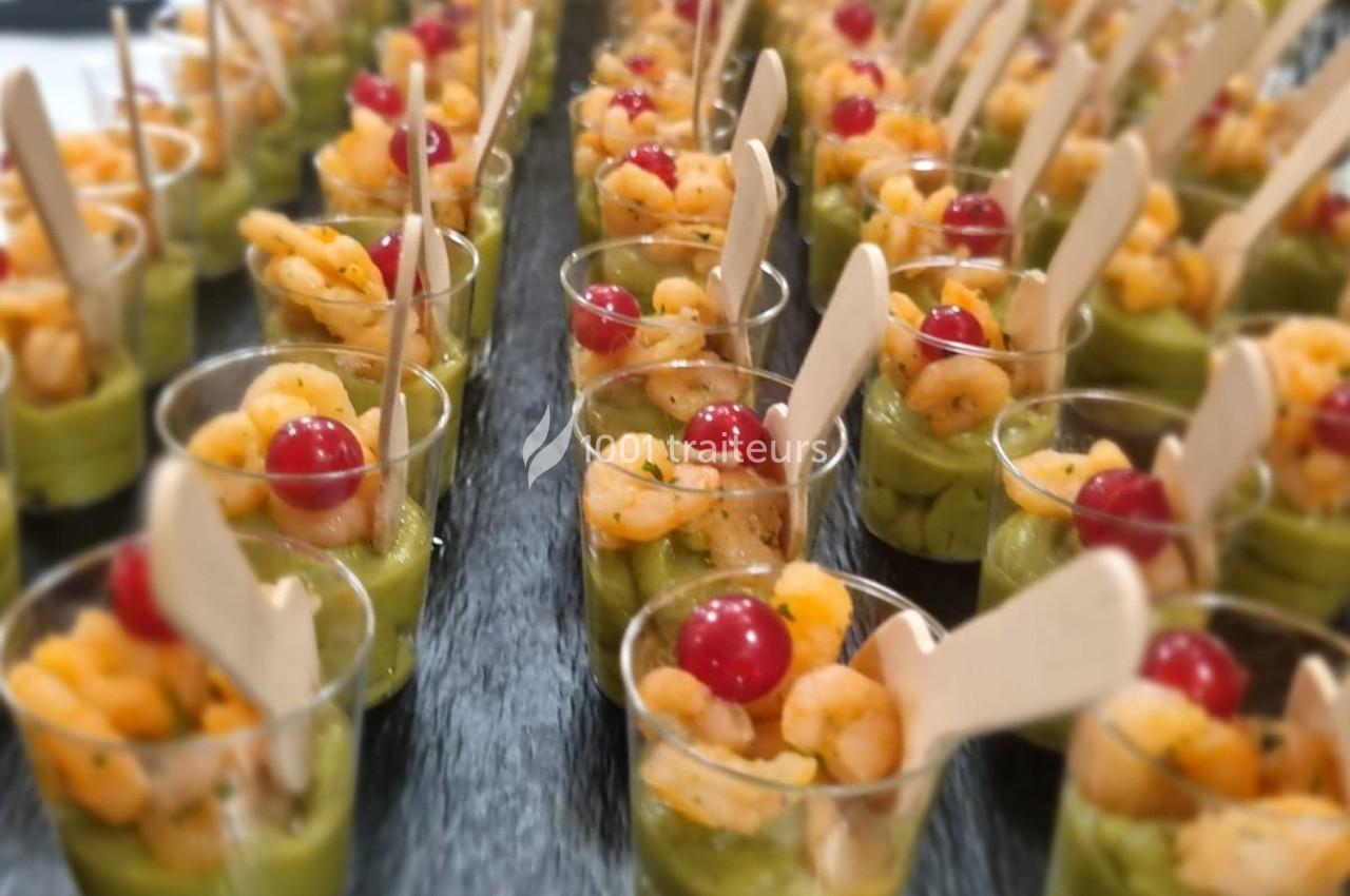 Verrines apéritives composées de crevettes, guacamole et groseilles, avec des cuillères en bois.