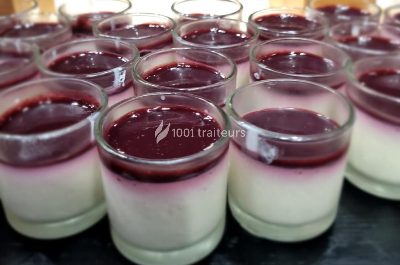 Verrines de panna cotta garnies d’un coulis rouge brillant disposées en rangées sur une surface sombre.
