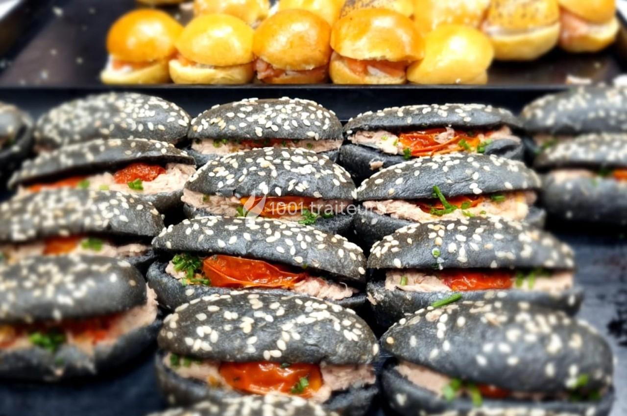 Sandwichs au pain noir garnis de thon, tomates confites et herbes, disposés sur un plateau devant des mini-burgers.
