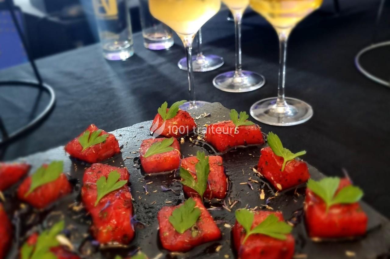 Bouchées de pastèque marinée garnies de feuilles de menthe, présentées sur une ardoise noire avec des verres en arrière-plan.