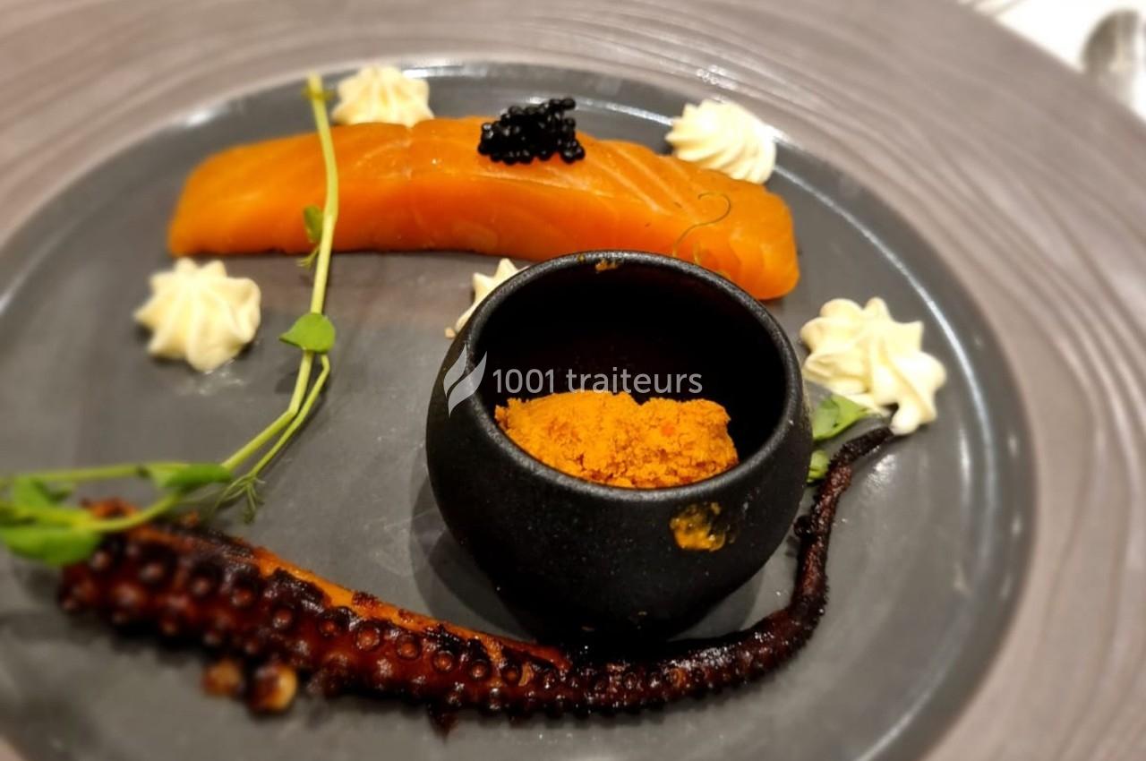 Assiette gastronomique avec saumon fumé, tentacule de poulpe grillé, épices dans un bol noir et décorations végétales.