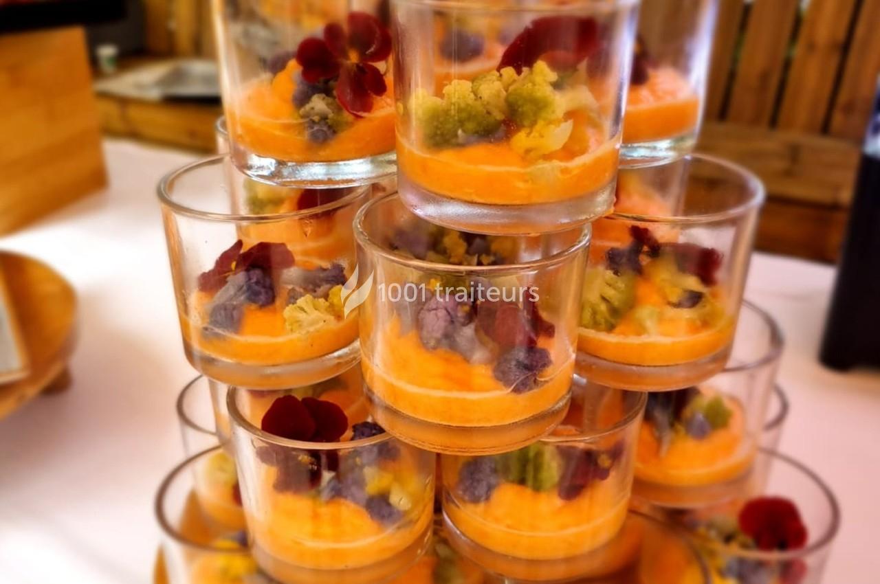 Verrines empilées contenant une mousse orange, décorées de légumes colorés et de fleurs comestibles.