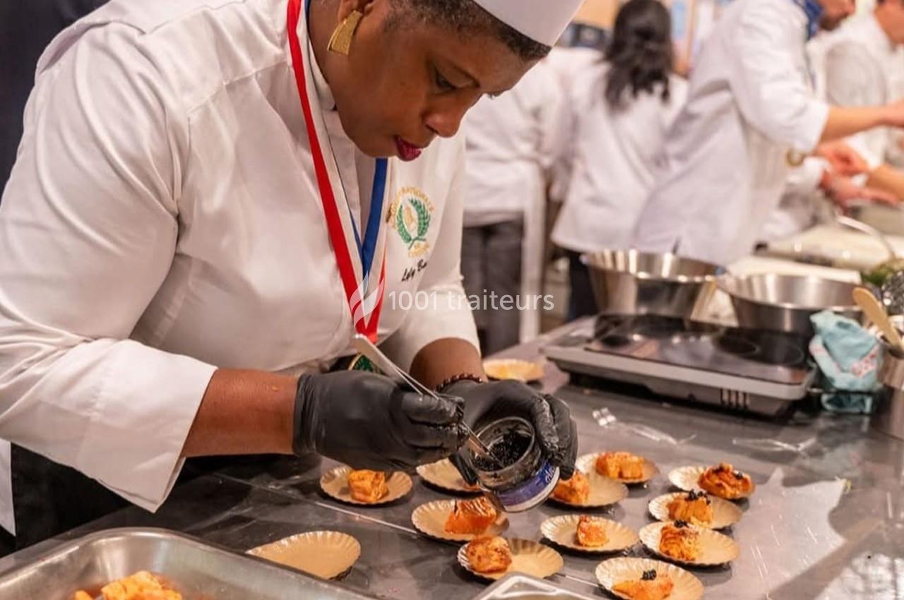 Une cheffe en tenue professionnelle dispose soigneusement un ingrédient sur des assiettes individuelles en cuisine.
