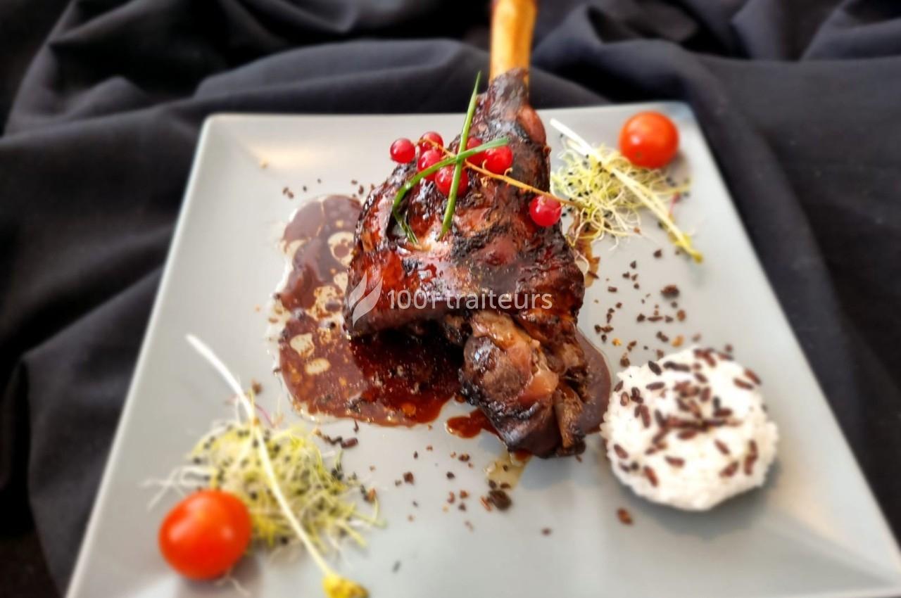 Plat de jarret d'agneau rôti avec sauce, décoré de groseilles, tomates cerises, pousses et accompagnement crémeux.