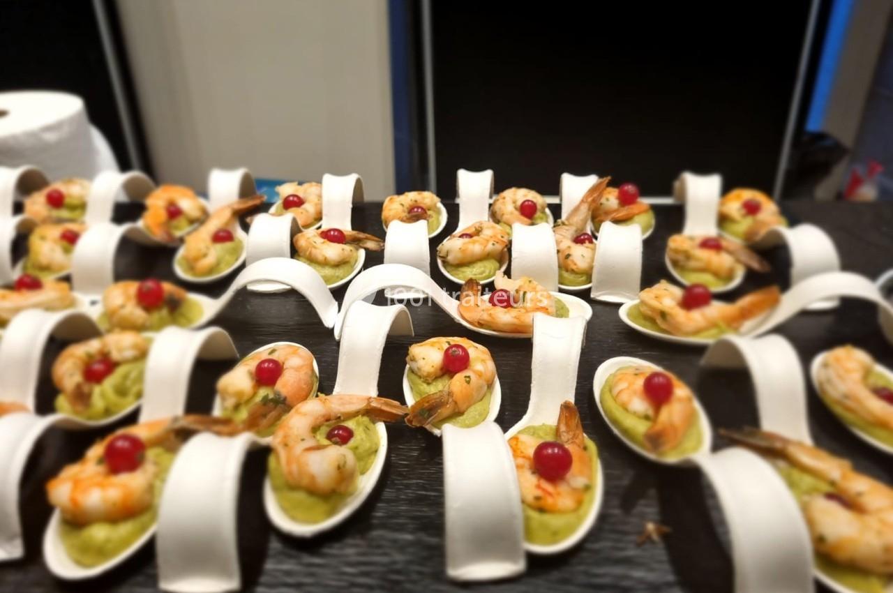 Cuillères en porcelaine garnies de crevettes, purée verte et baies rouges, disposées sur une table noire.