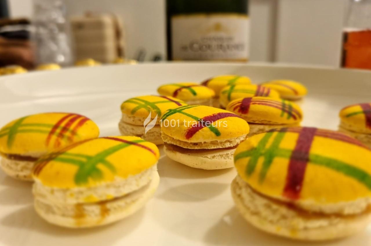 Macarons jaunes décorés de motifs colorés, disposés sur une assiette blanche avec une bouteille en arrière-plan.