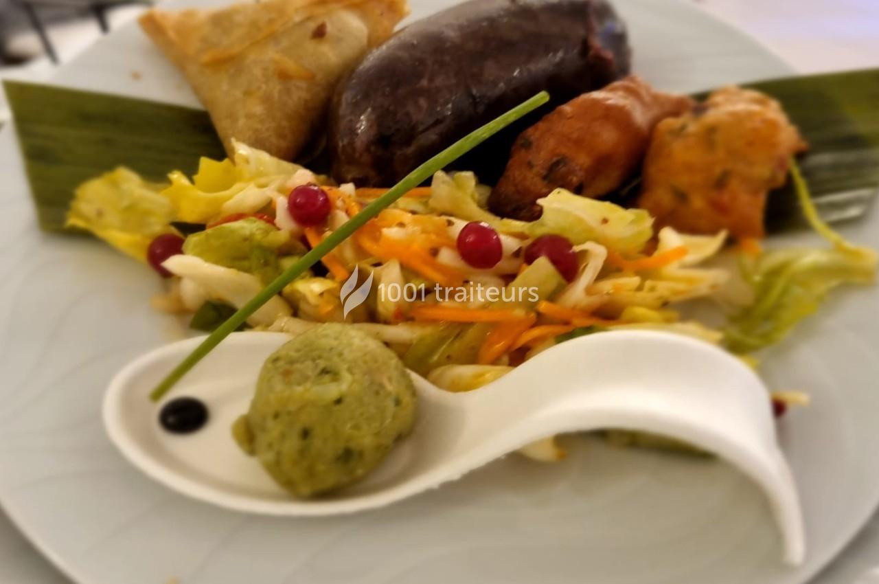 Assiette composée de samoussa, boudin, beignet, salade colorée et boule verte sur une cuillère blanche.