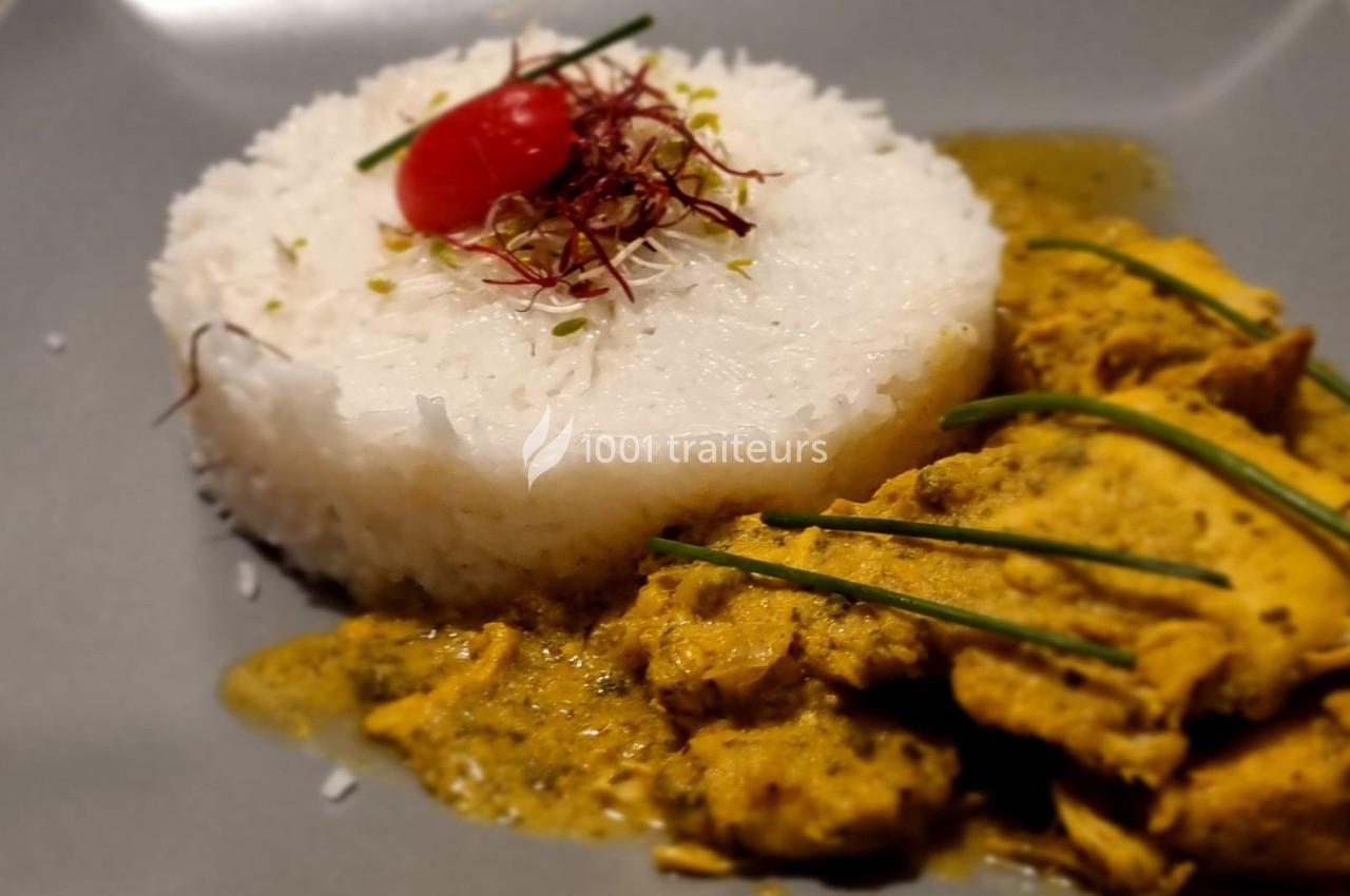 Assiette avec du riz blanc moulé, garni d'une tomate cerise et d'herbes, accompagné de poulet en sauce jaune.