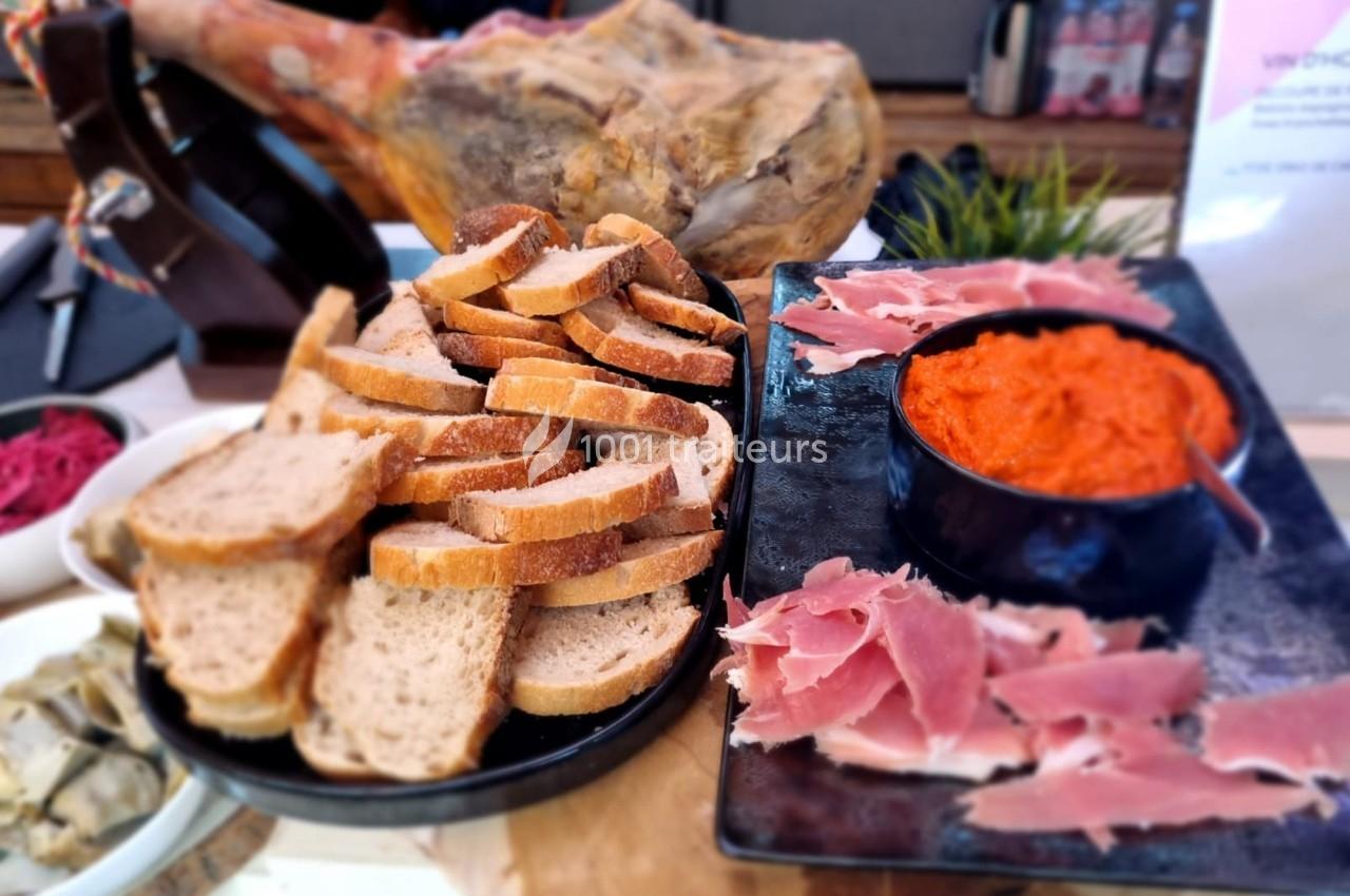 Plateau avec tranches de pain, jambon cru, bol de sauce rouge et arrière-plan flou avec un jambon entier.