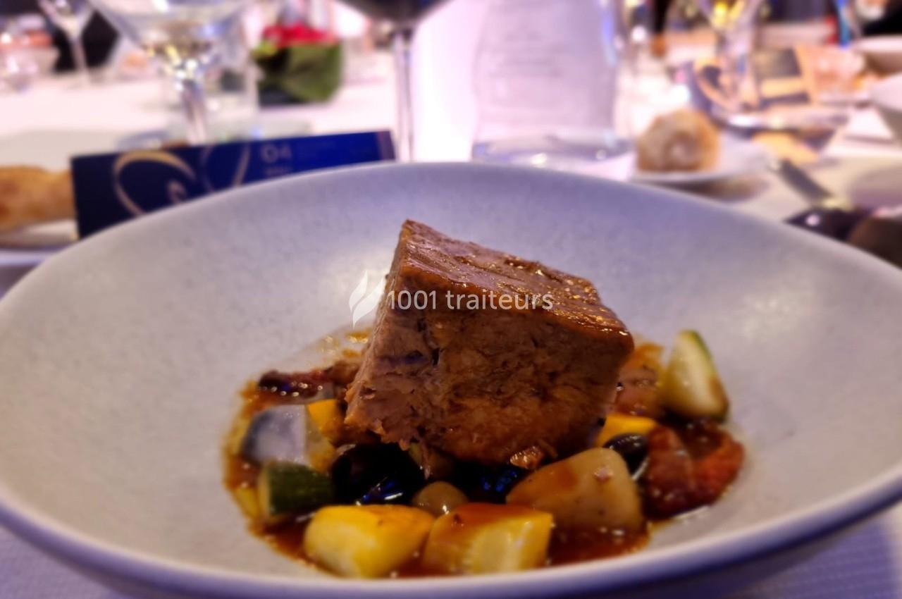 Plat gastronomique composé d'un morceau de viande braisée accompagné de légumes et d'une sauce dans une assiette blanche.