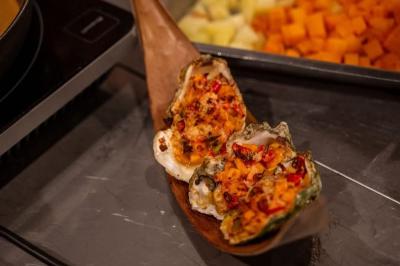 Miniature Traiteur Savigny-le-Temple (Seine-et-Marne) - Nos Tendances Traiteur #88 Huîtres gratinées garnies de fromage et épices, présentées sur un plateau en bois, avec légumes en arrière-plan.