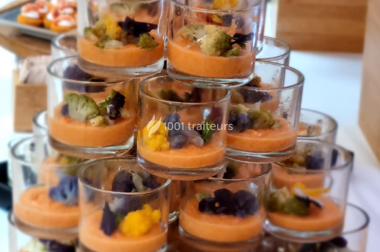 Verrines empilées contenant une mousse orange garnie de fleurs comestibles et de légumes colorés.