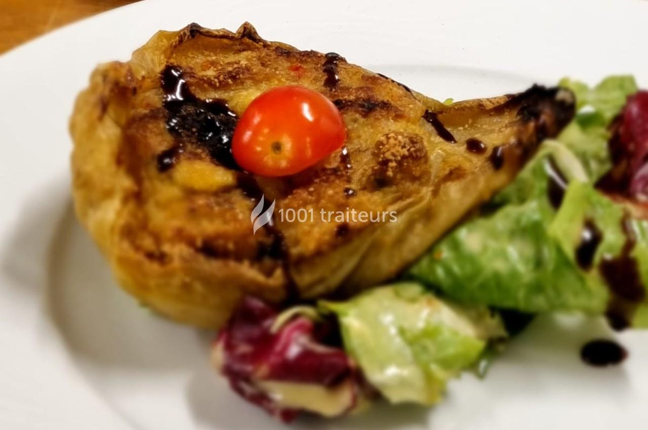 Part de tarte feuilletée garnie, décorée d'une tomate cerise et accompagnée de salade verte et rouge.
