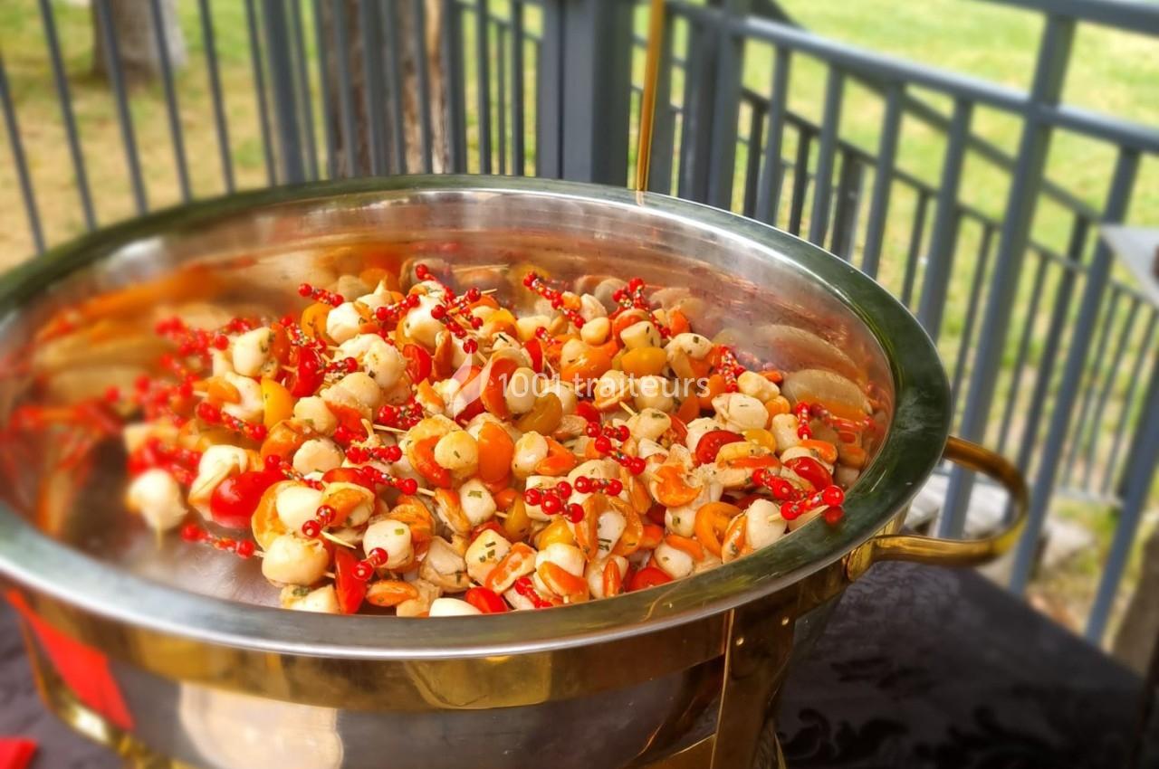 Plat en inox contenant une salade colorée avec des légumes, des baies rouges et des herbes, posé sur une table en extérieur.