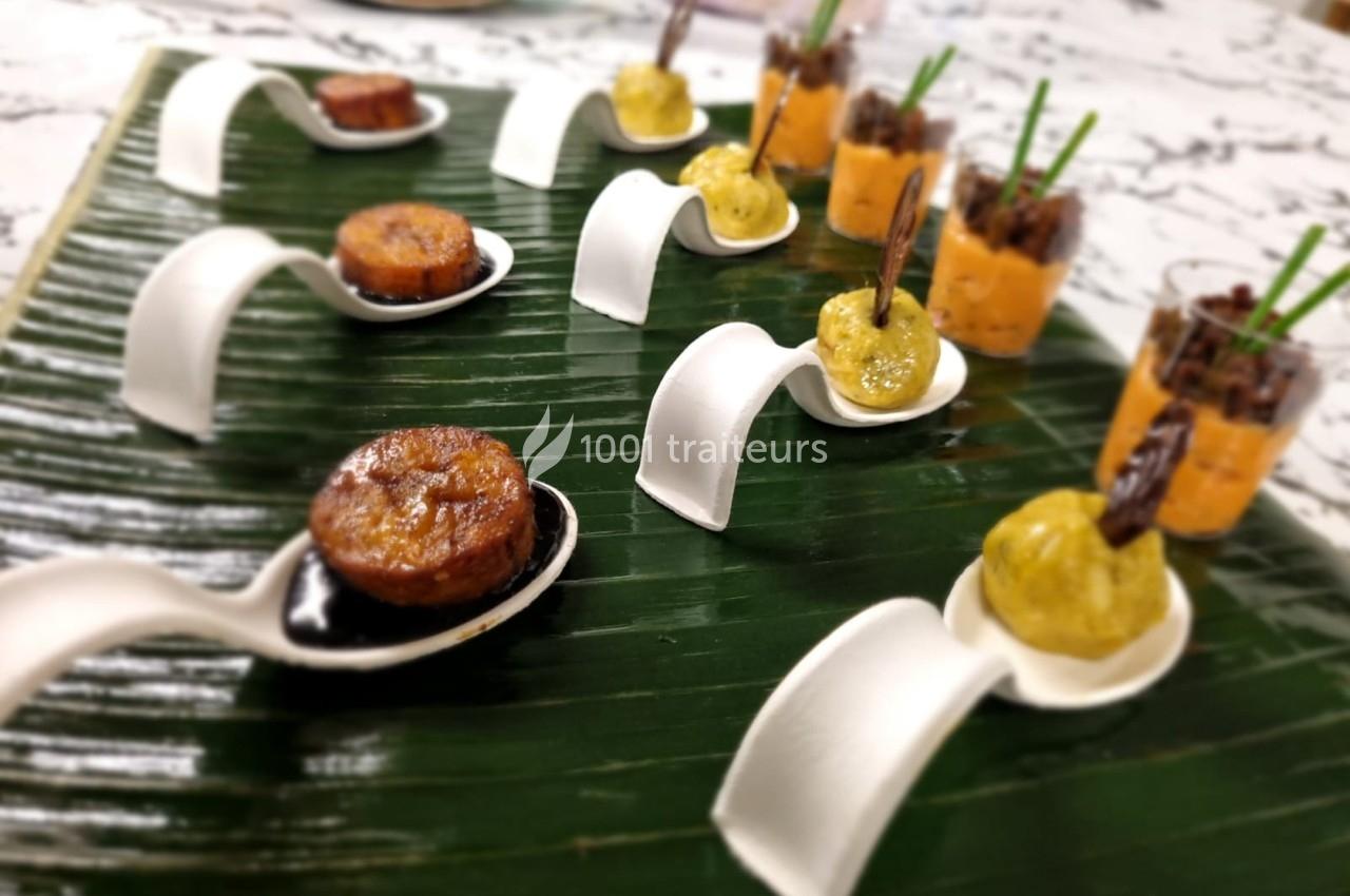 Assortiment de bouchées gastronomiques présentées sur des cuillères et verrines, disposées sur une feuille verte.