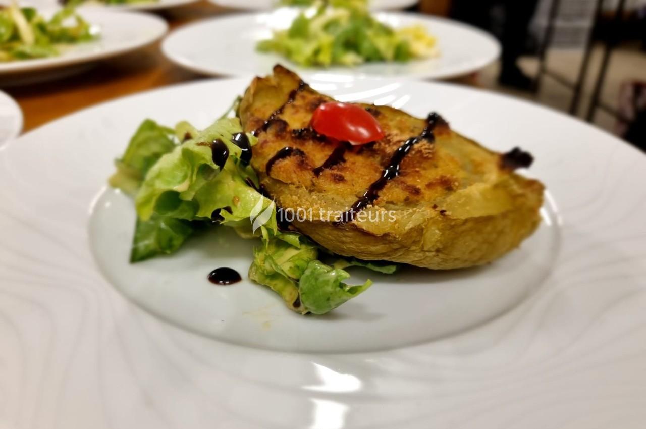 Assiette contenant une demi-pomme de terre gratinée, accompagnée de salade verte et décorée d'une tomate cerise.