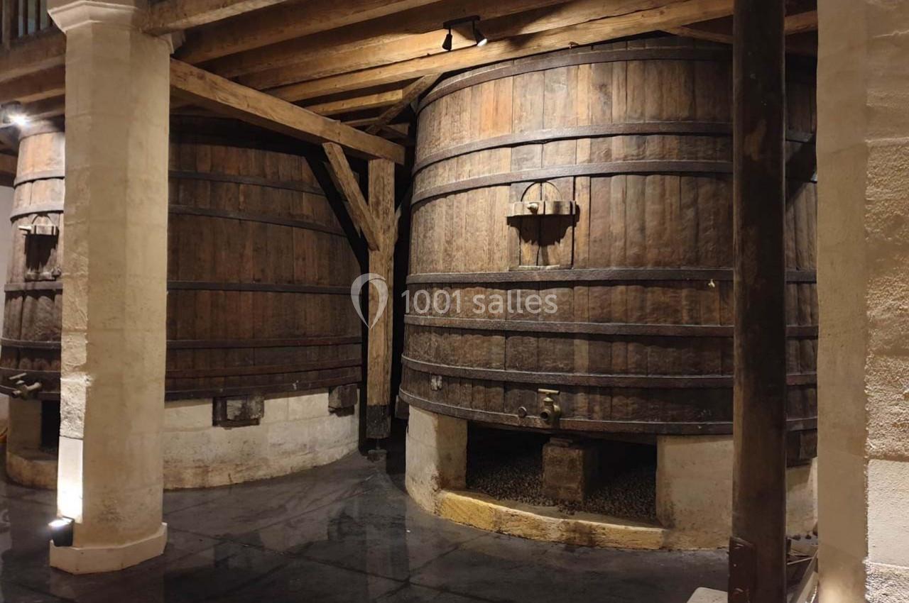 Deux grands tonneaux en bois dans une cave voûtée avec un sol en pierre sombre.